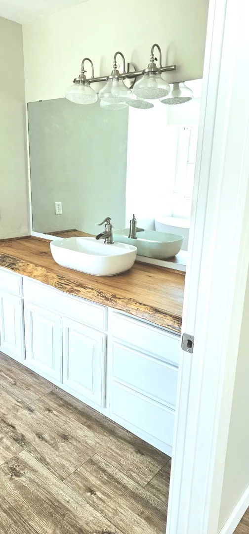 Wood-finish flooring complementing a vanity with white cabinetry and a live-edge wood countertop
