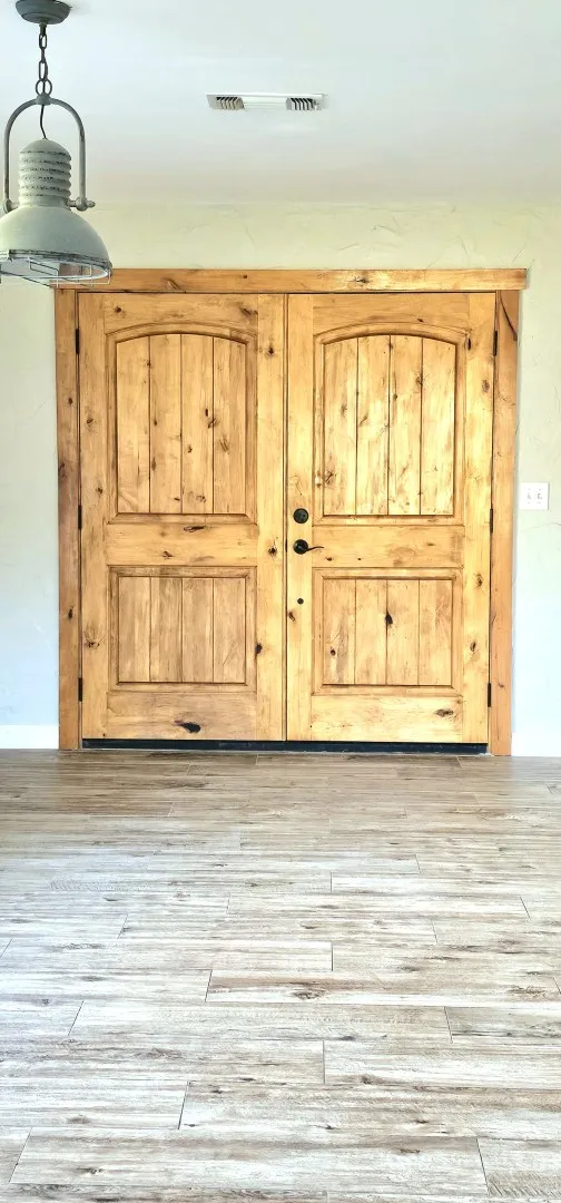 Double rustic wood doors with arched paneling, dark hardware, and light wood-finish flooring