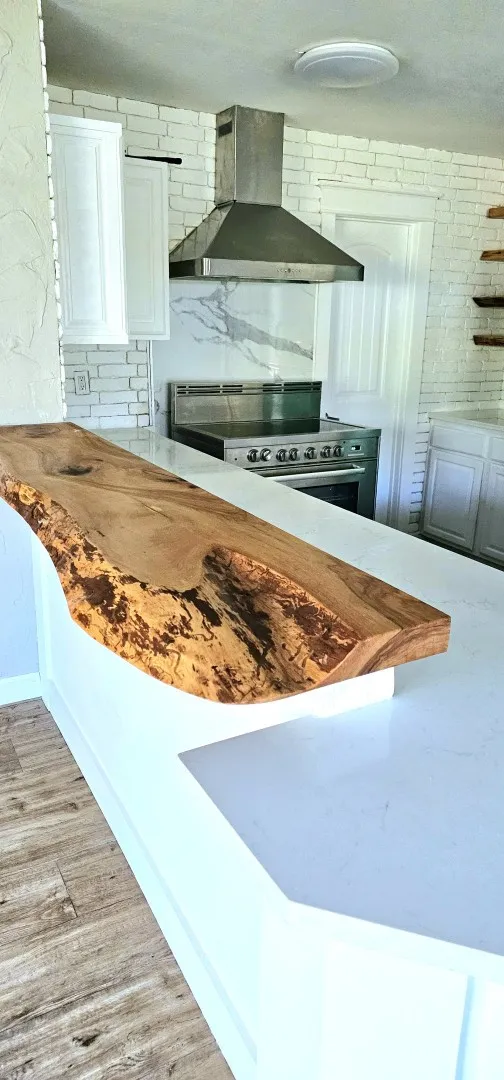 Kitchen featuring a live edge wood-finish bar top, white countertops, stainless steel range with hood, white brick-patterned tile backsplash, and wood-finish flooring