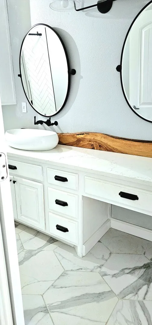 Dual oval mirrors with matte black frames above a white vanity with integrated cabinetry