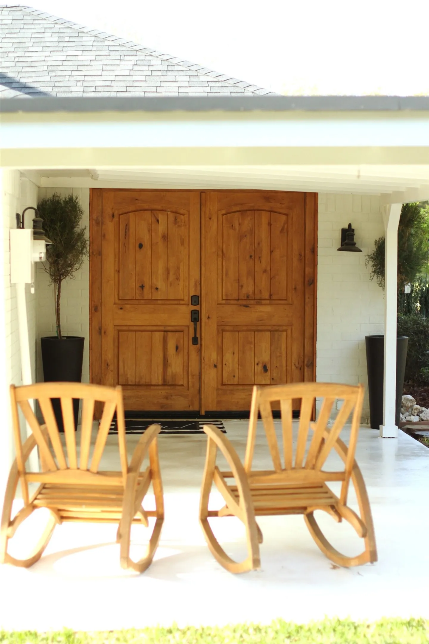 White brick exterior with a covered porch featuring natural wood double entry doors