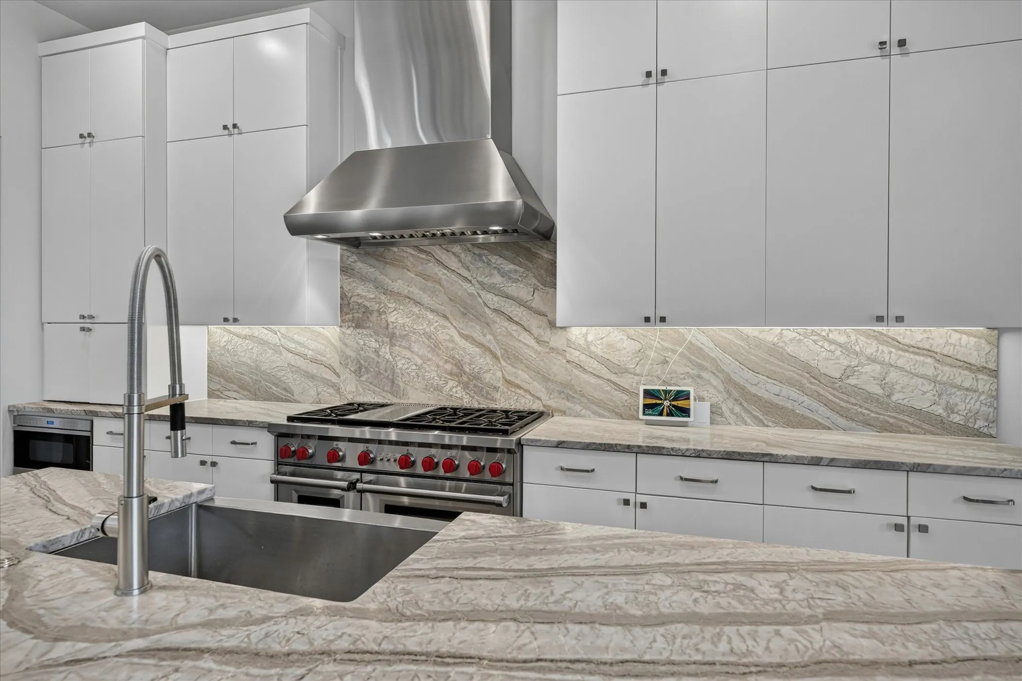 Gourmet kitchen featuring a stainless steel range with a matching range hood, ample white cabinetry, under-cabinet lighting, a large stainless steel sink, and extensive stone countertops with a matching backsplash