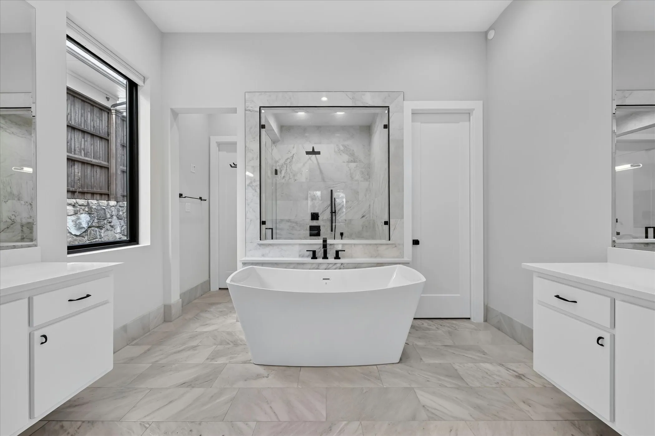 Contemporary bathroom featuring a freestanding tub, a spacious glass-enclosed shower with tile surround, dual floating vanities with white countertops, and large format tile flooring