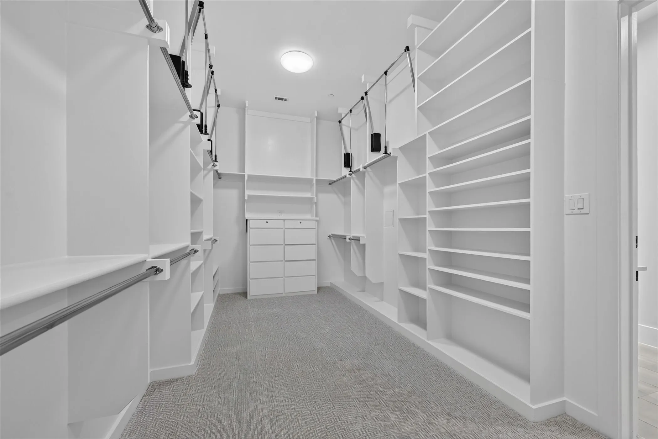 Expansive walk-in closet featuring extensive built-in shelving, hanging rods, and a central dresser unit