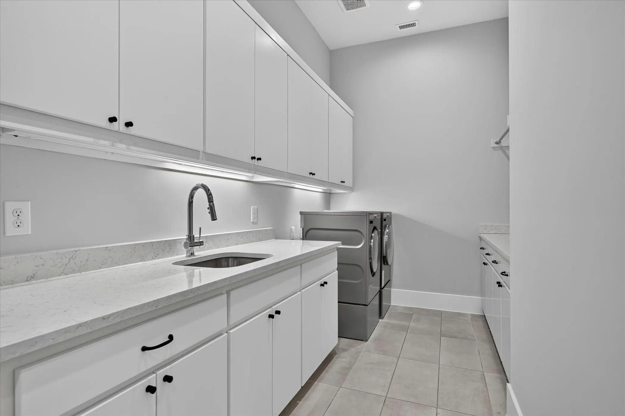 Laundry room featuring extensive white cabinetry, light-toned countertops, an undermount sink with a gooseneck faucet, tiled flooring, and recessed lighting