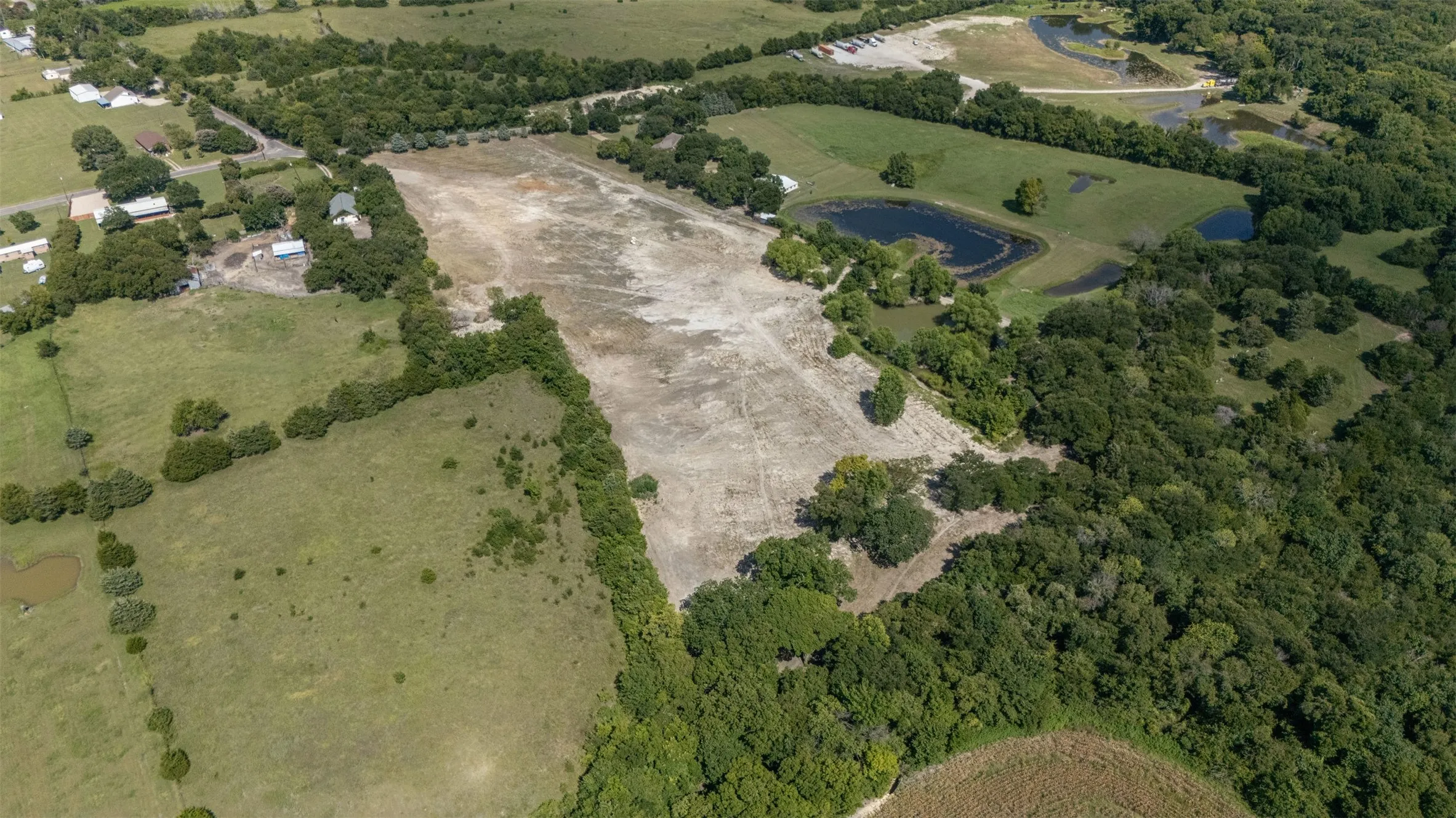 Expansive acreage featuring a substantial cleared area, surrounding green pastures, dense tree lines, and multiple water features