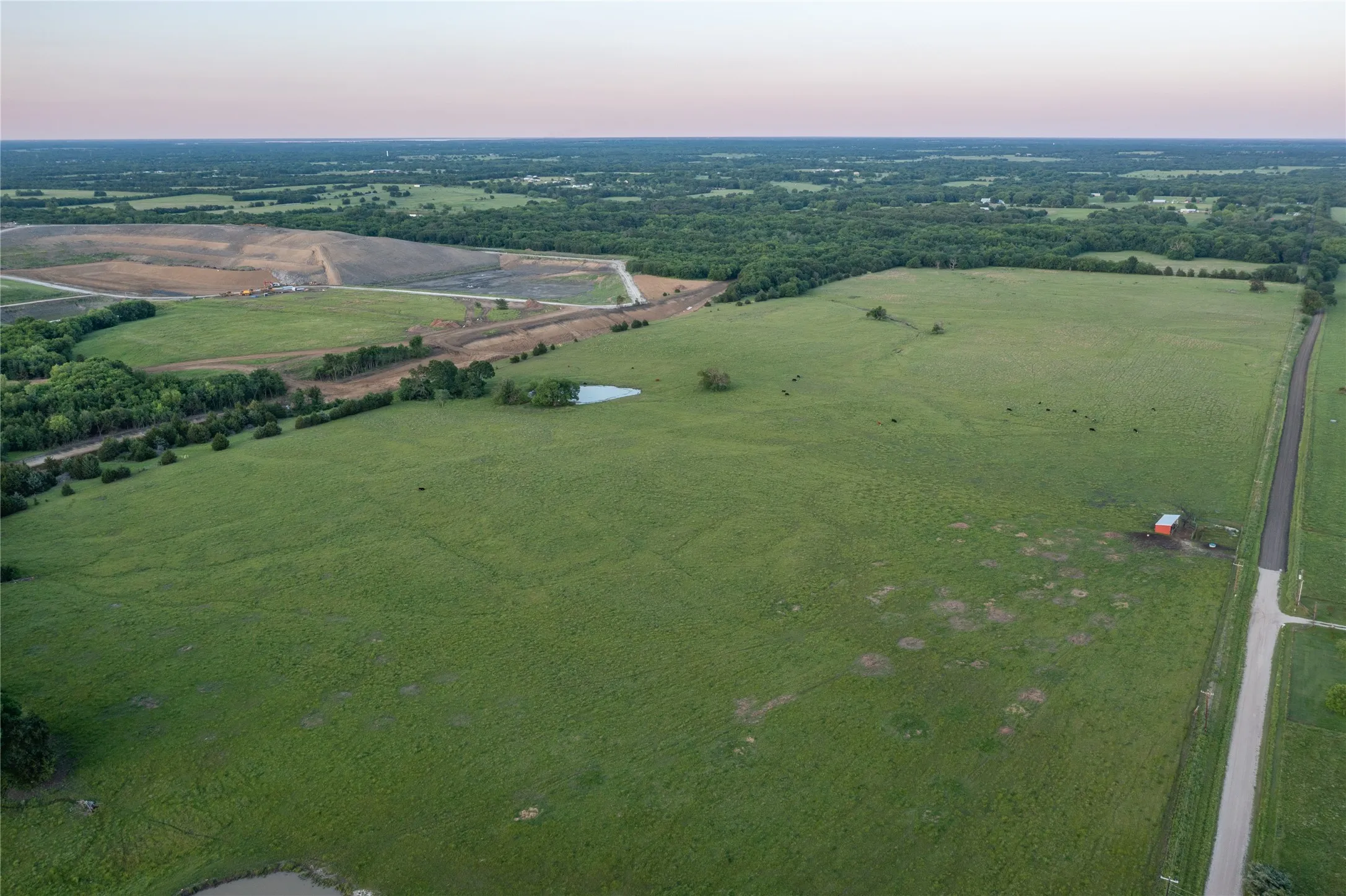 Expansive green pastureland with multiple ponds and distant wooded areas