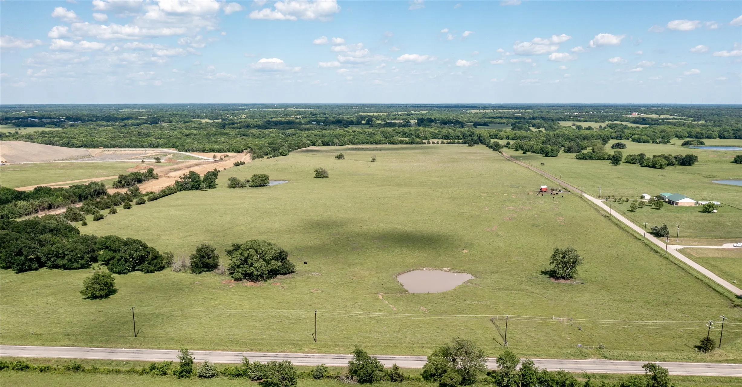 Expansive rural property featuring an open field with scattered trees, a natural pond, and a paved road bordering the perimeter