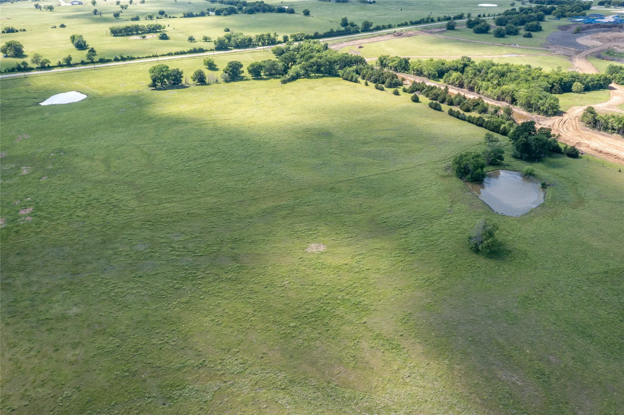 Expansive green fields with two ponds, scattered trees, and a distant paved road