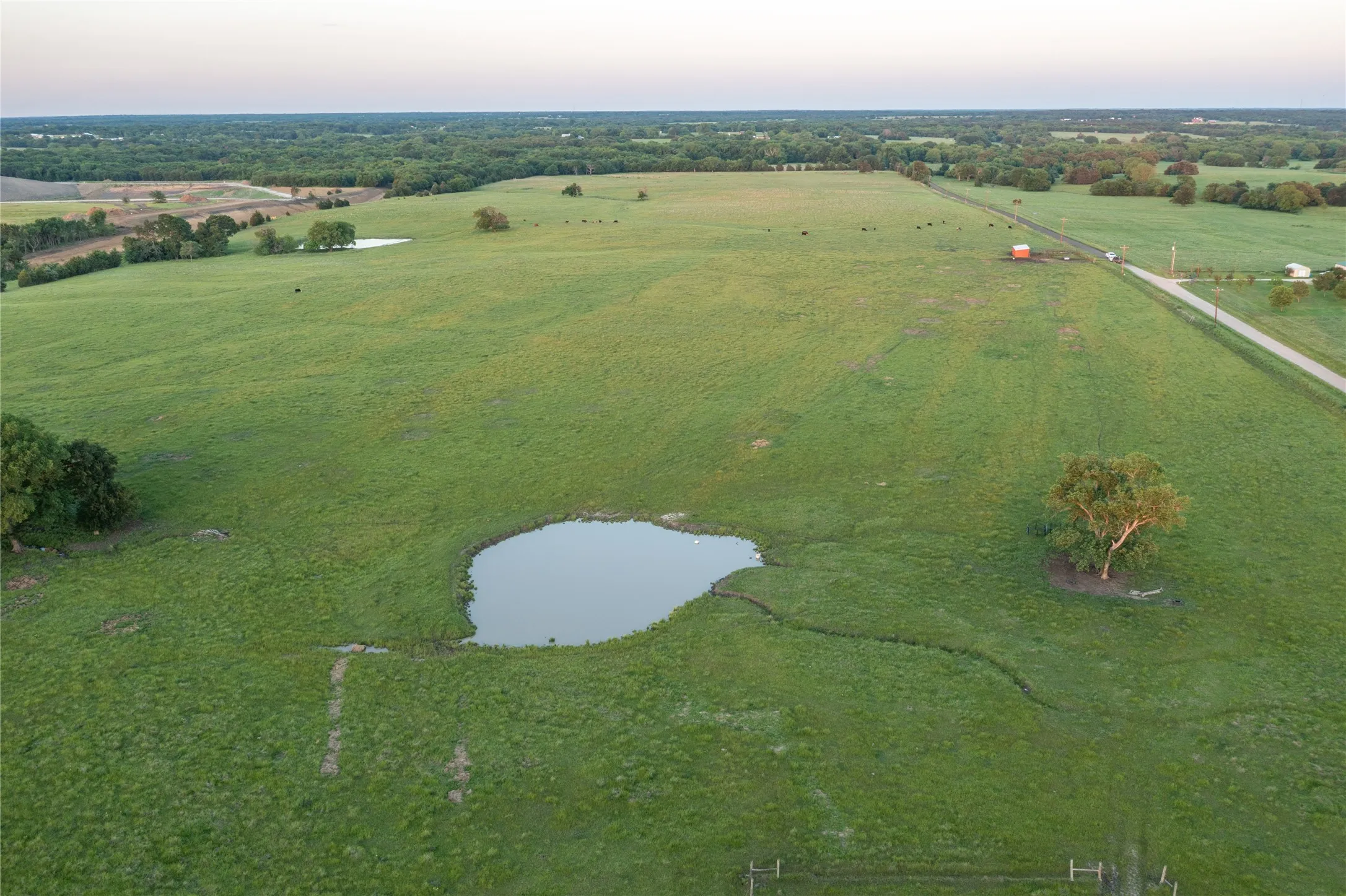 Expansive green acreage featuring multiple ponds, scattered mature trees, and an unpaved road