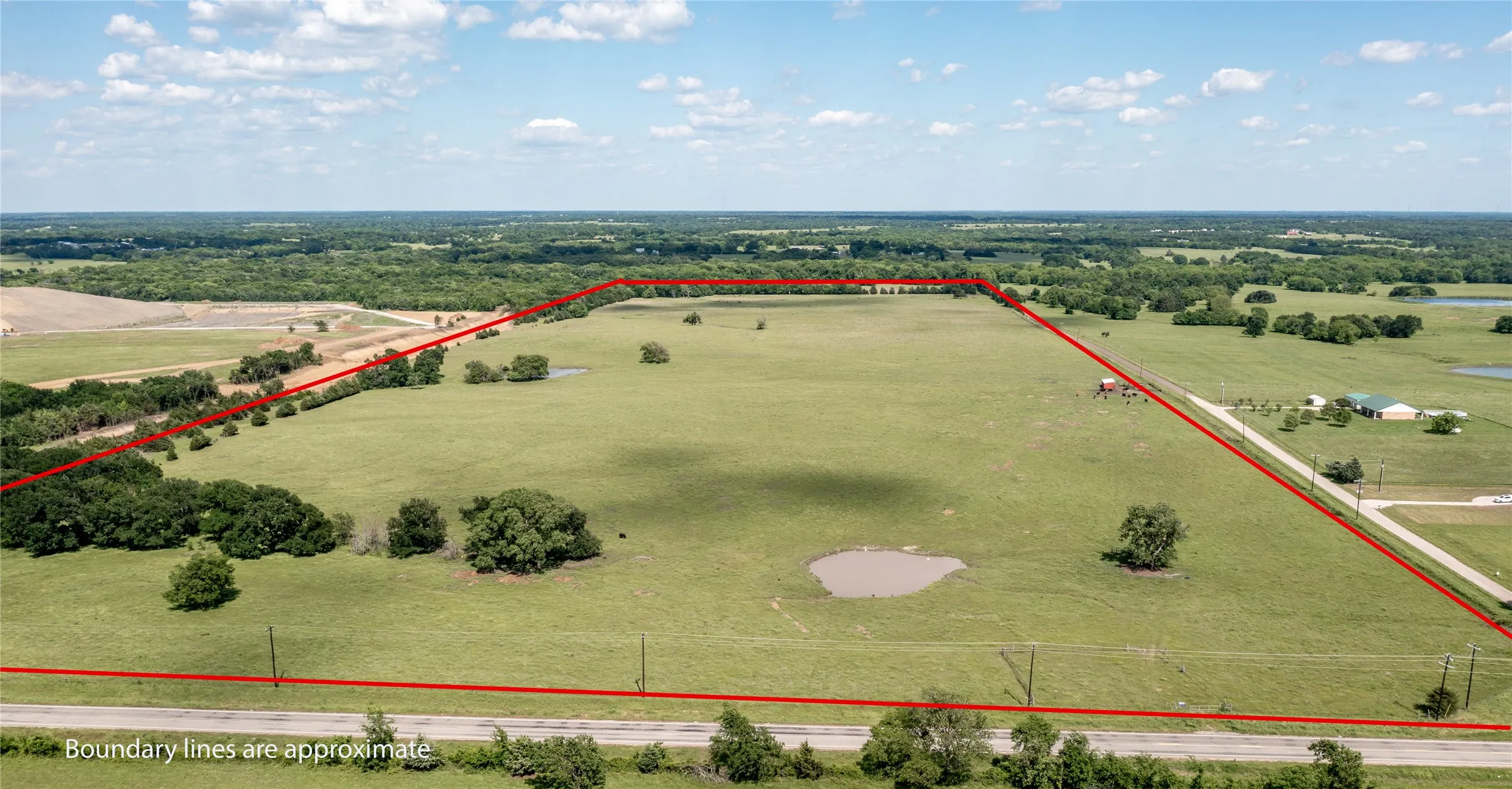 Expansive acreage featuring open pastureland, a natural pond, scattered mature trees, and direct road frontage