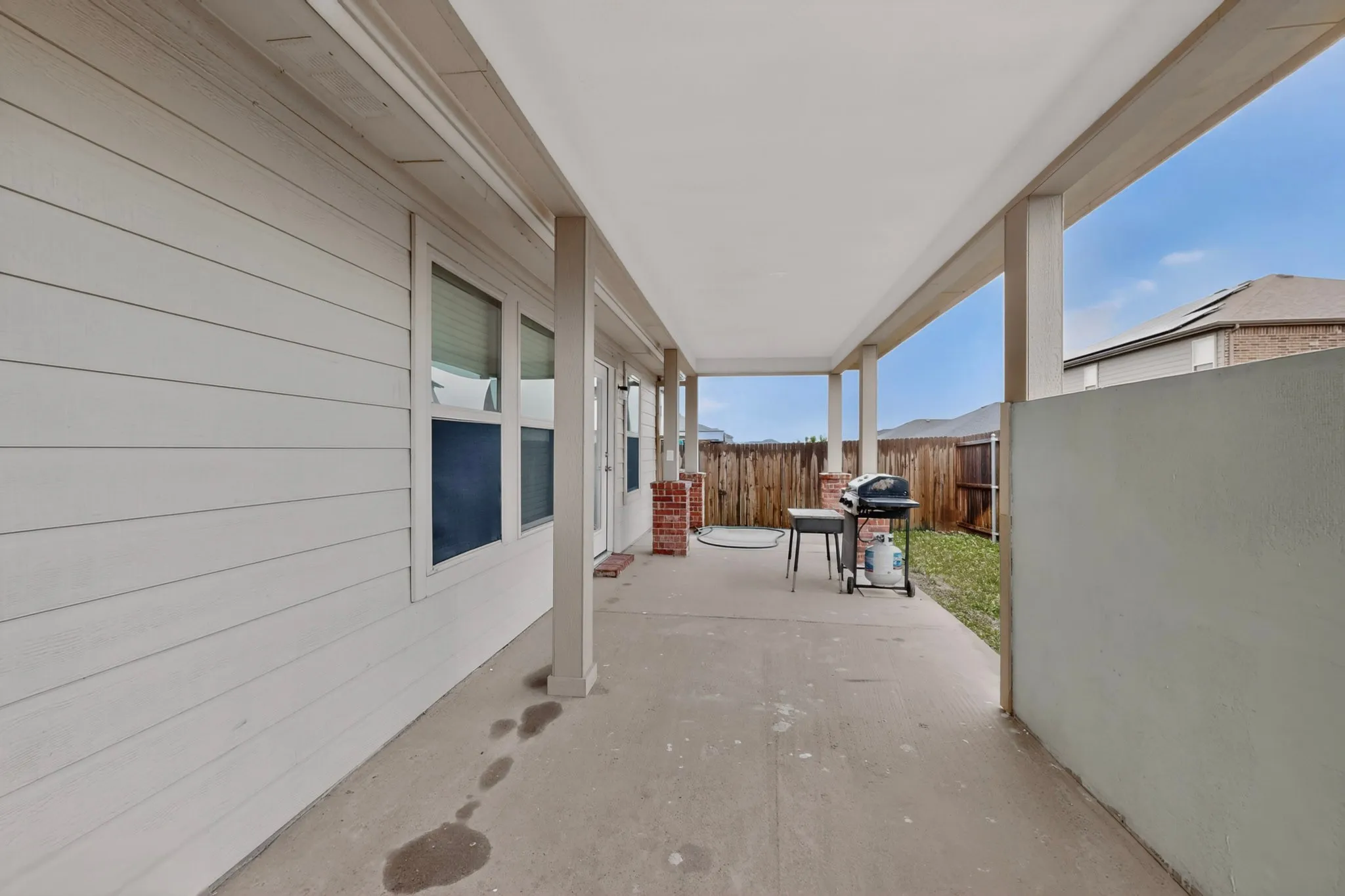 Covered patio featuring a concrete slab, white siding, and brick accents