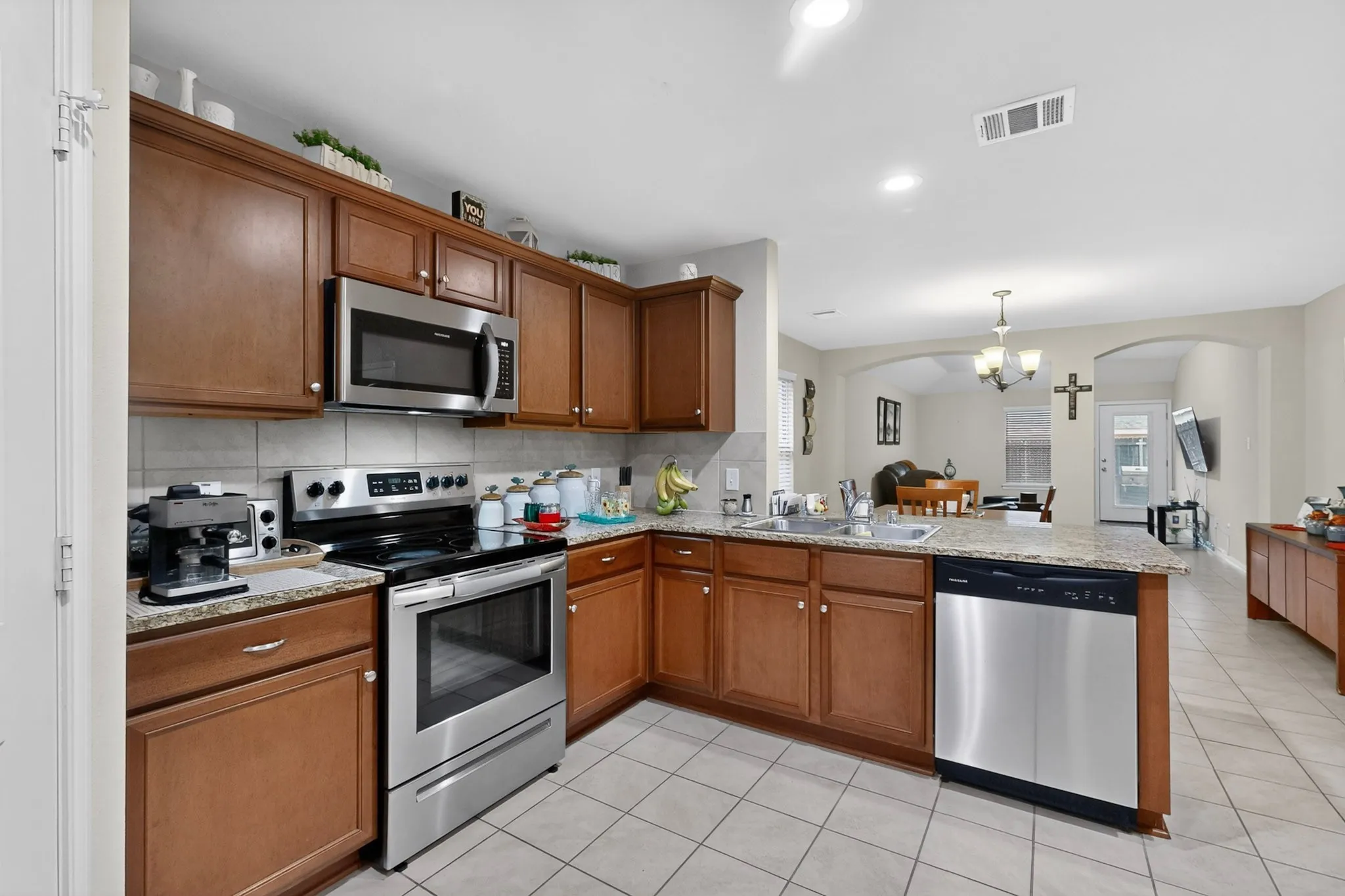 Kitchen featuring warm wood-finish cabinetry, stainless steel appliances, granite-style countertops, and a tile backsplash