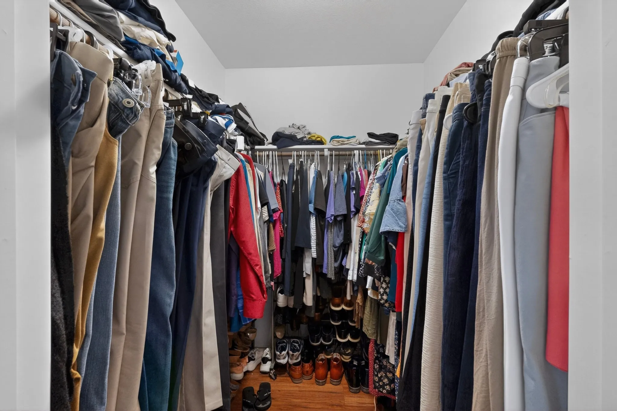Walk-in closet featuring wood-finish flooring, white walls, and comprehensive metal hanging rods and shelving