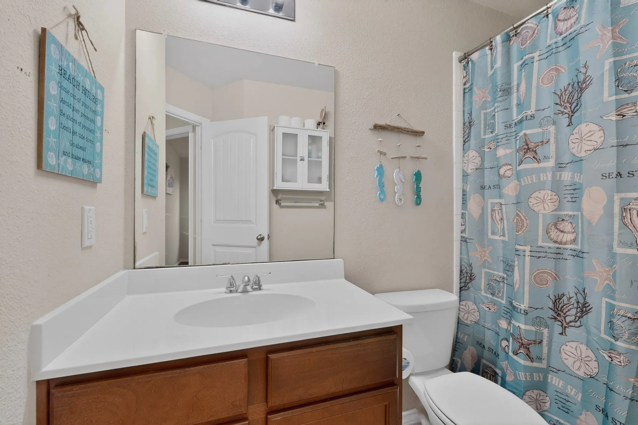 Bathroom featuring a wood-finish vanity with a white countertop and integrated sink, a large wall mirror, and a built-in shower/tub combination