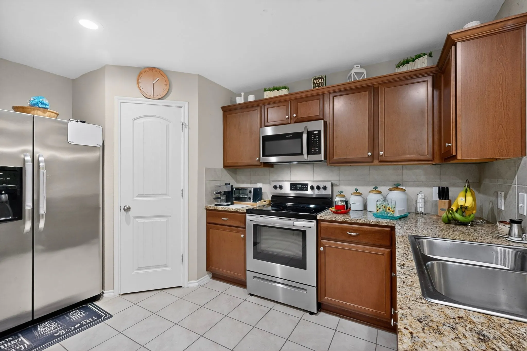 Kitchen featuring granite-style countertops, stainless steel appliances, wood-finish cabinetry, and a tile backsplash