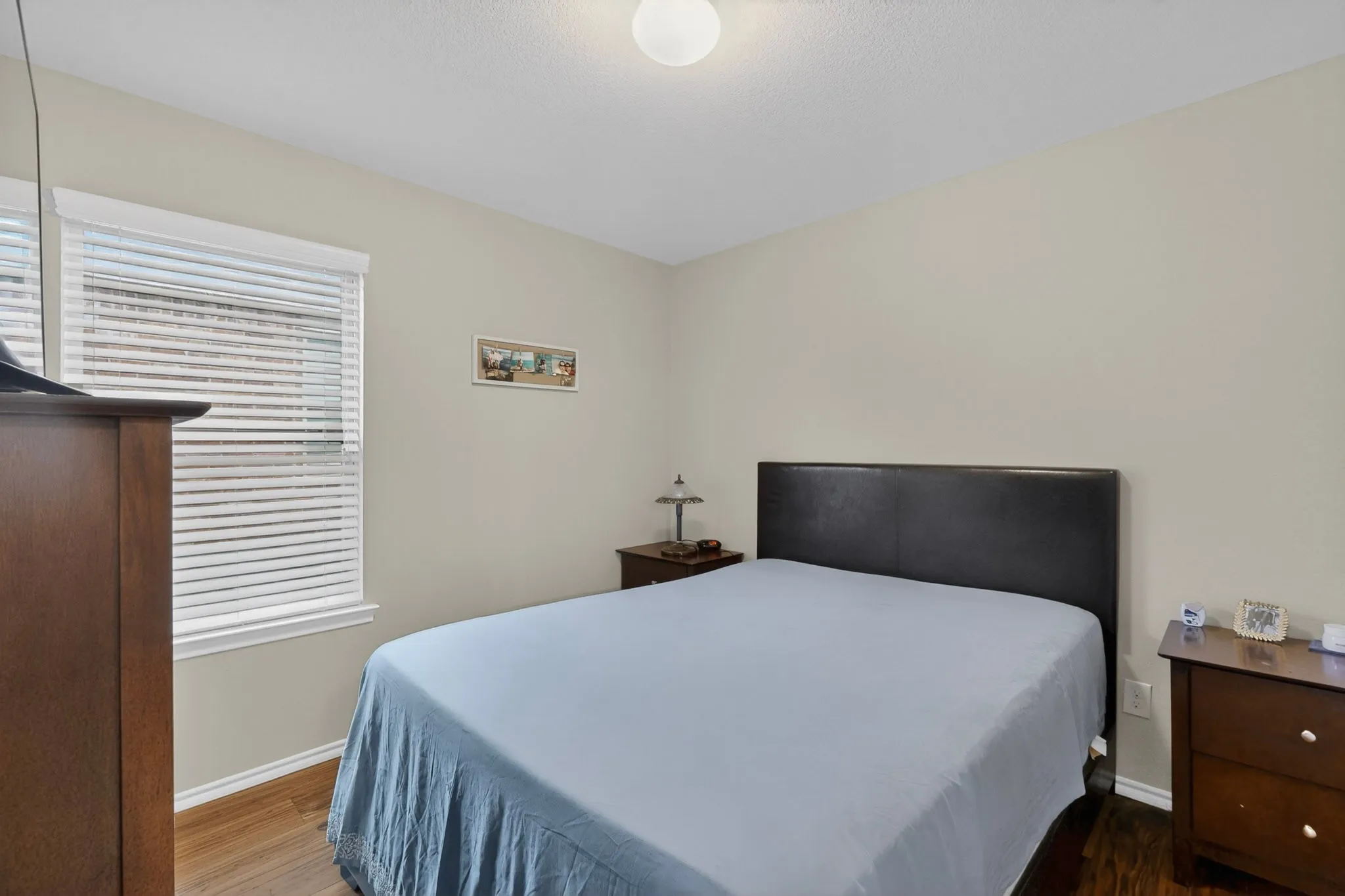 Bedroom featuring wood-finish flooring and a single window with horizontal blinds