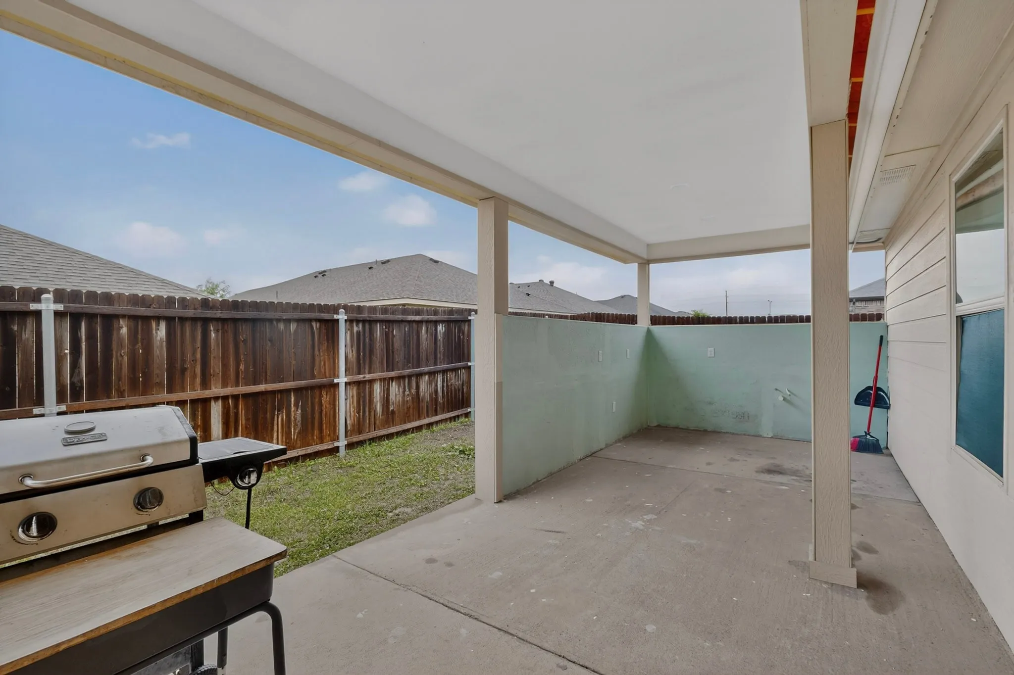 Covered concrete patio with a painted privacy wall and a wood fence border