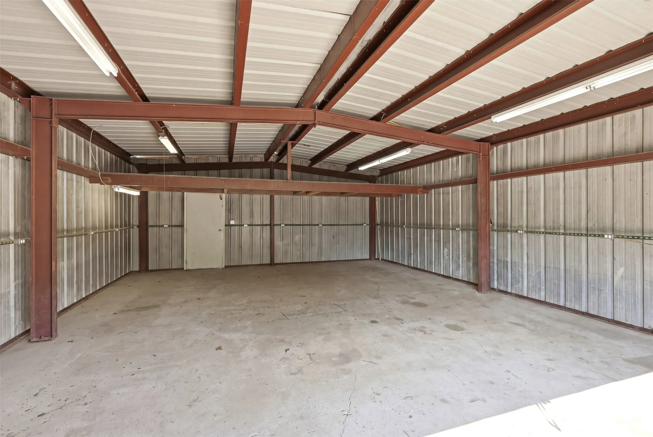 Spacious industrial-style interior with concrete flooring and corrugated metal walls and electrical outlets surrounding