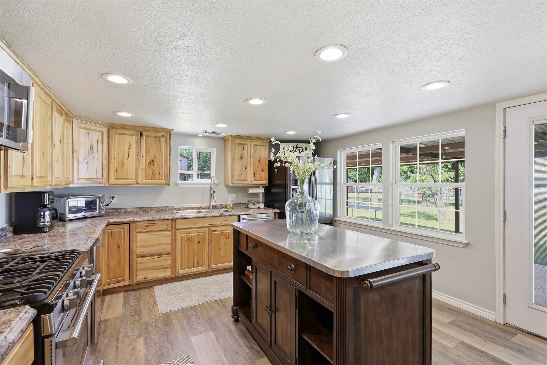 Kitchen featuring recessed lighting, a central island with a metal countertop, wood-finish flooring, a stainless steel gas range, and multiple windows