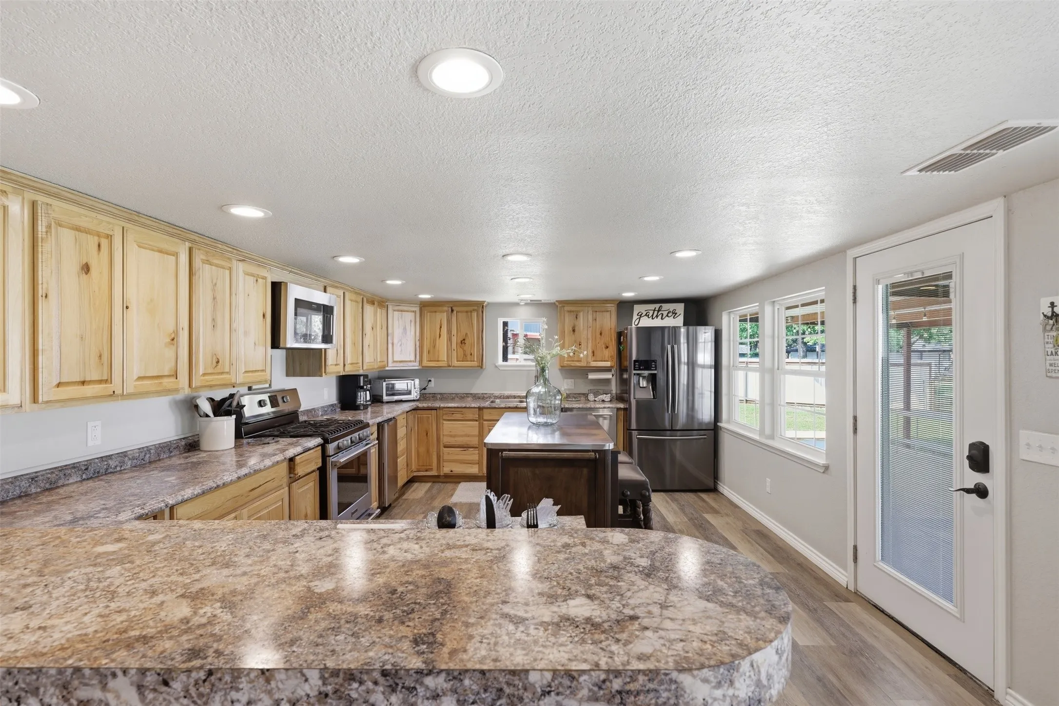 Expansive kitchen featuring wood cabinetry, stone-look countertops, and stainless steel appliances