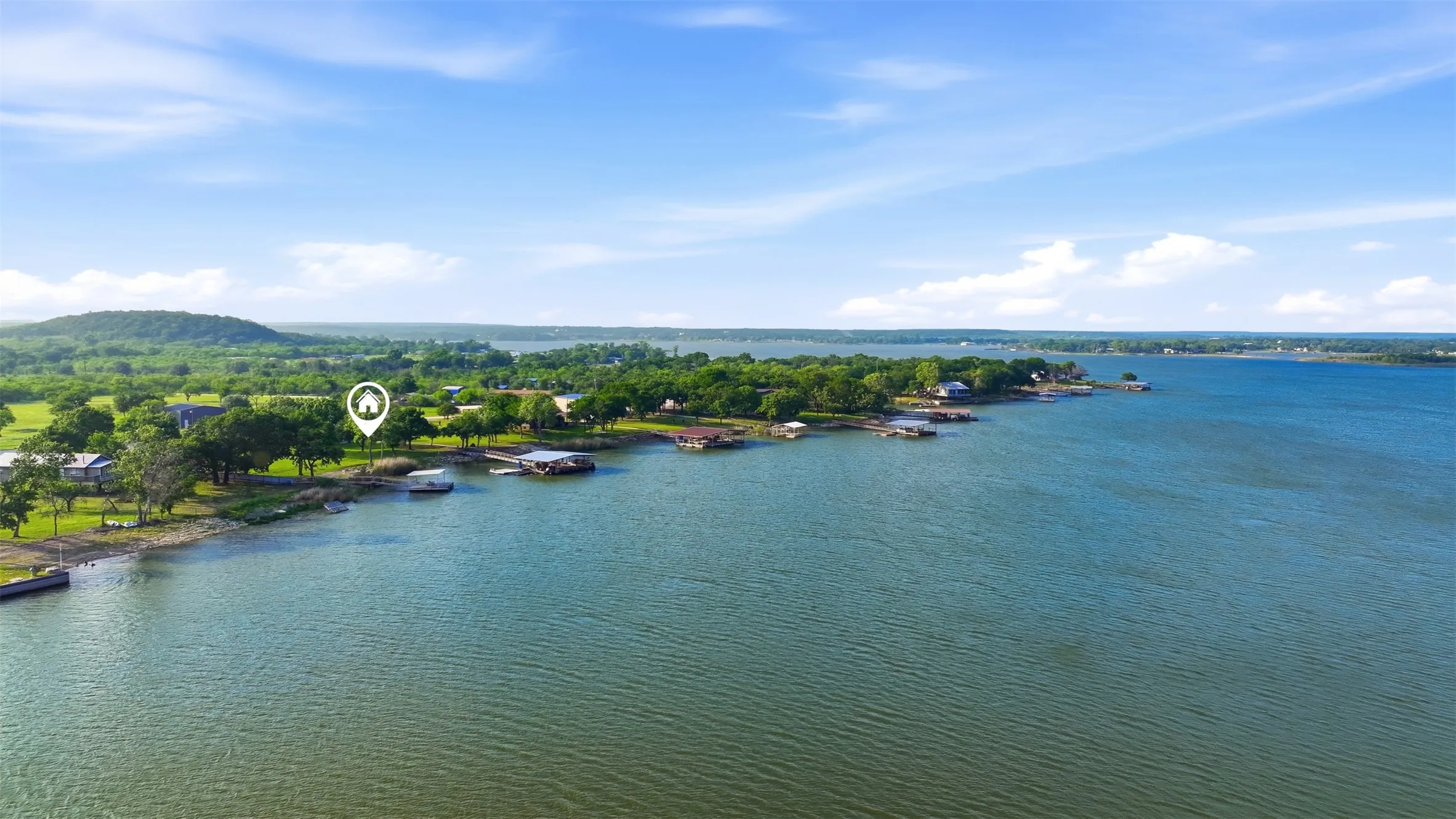 Waterfront property featuring a prominent shoreline, mature trees, and a clear blue sky
