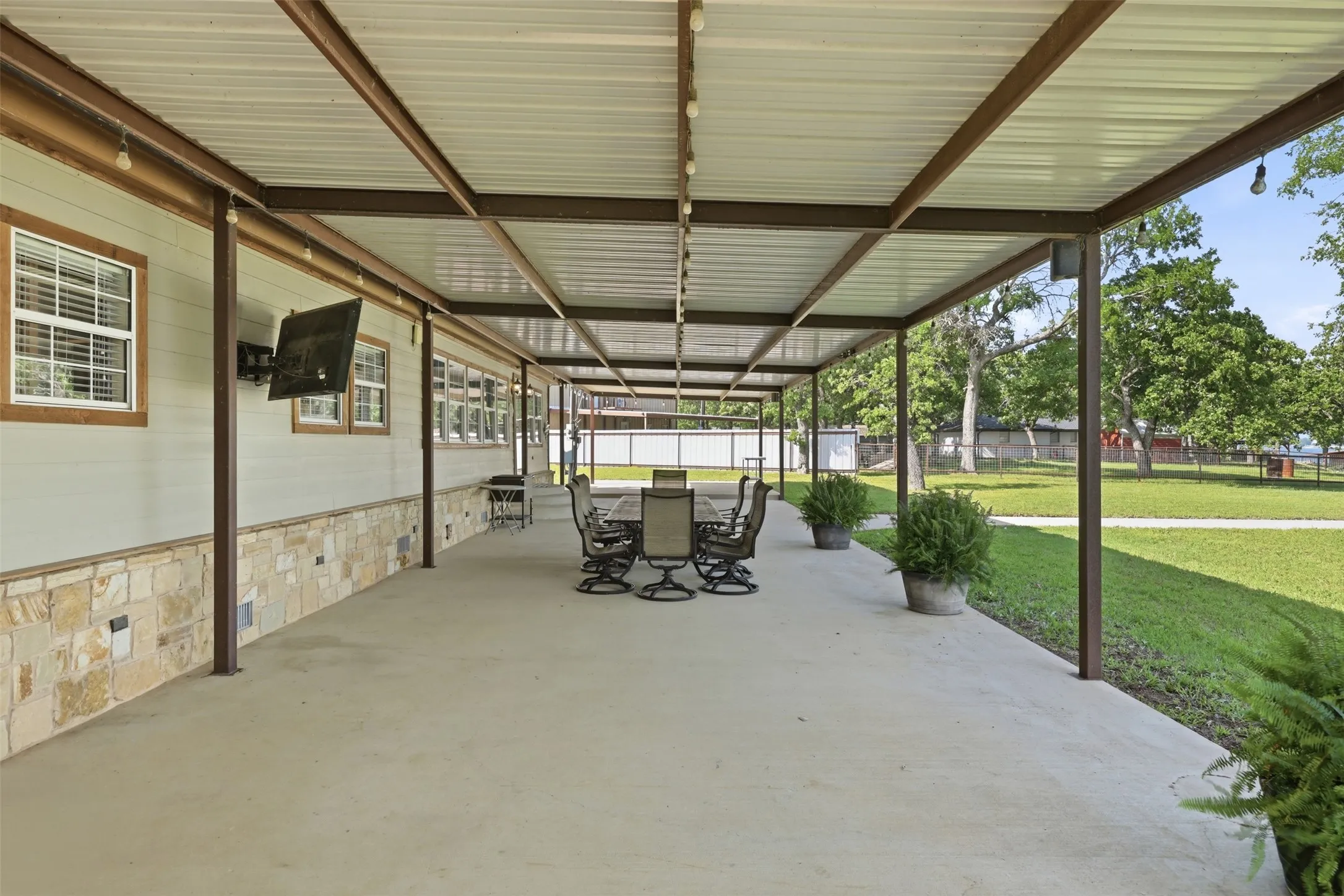 Expansive covered patio featuring a metal roof structure, concrete flooring, stone veneer detailing, and white siding