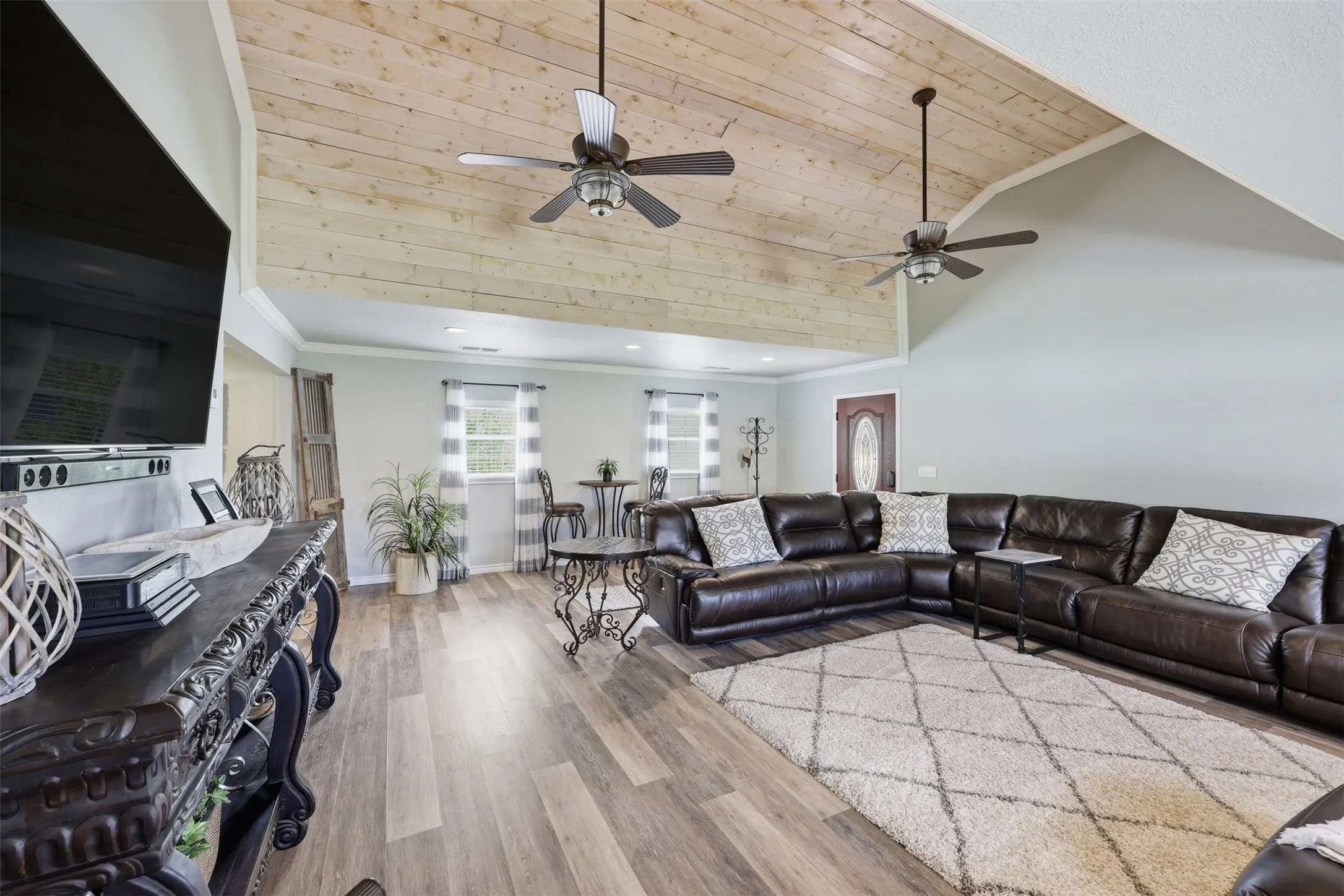 Spacious living area featuring a vaulted wood-plank ceiling, wood-finish flooring, two ceiling fans, and multiple windows with vertical blinds