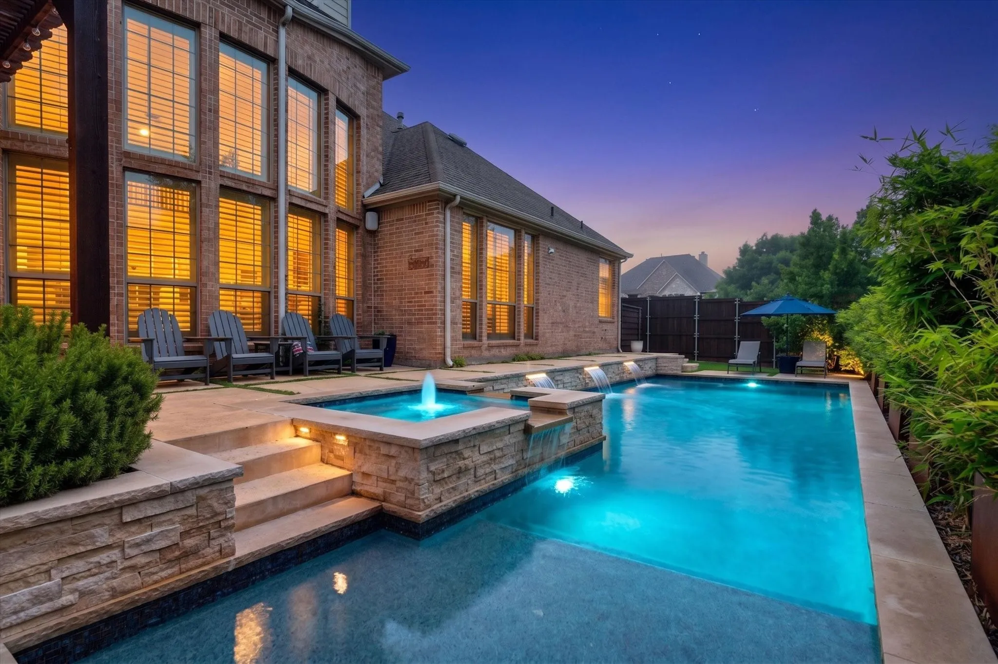 Evening lighting transforms the backyard into a private resort with a glowing pool, spa, patio, and outdoor entertaining space.