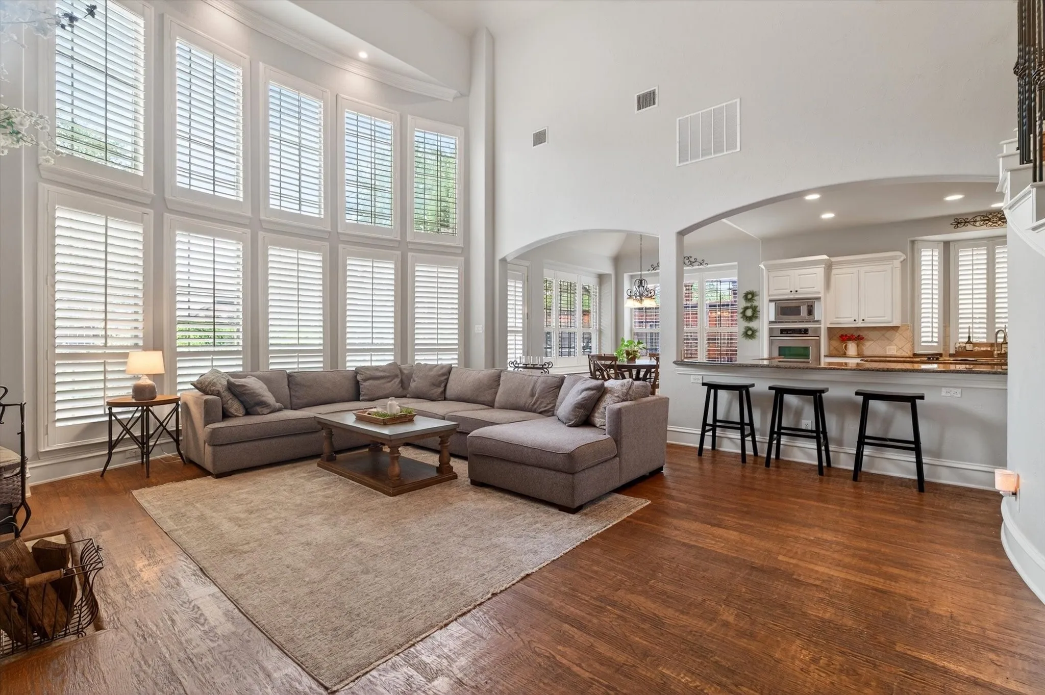 Natural light pours through two-story windows, highlighting the open flow between the living room, kitchen, and breakfast area.