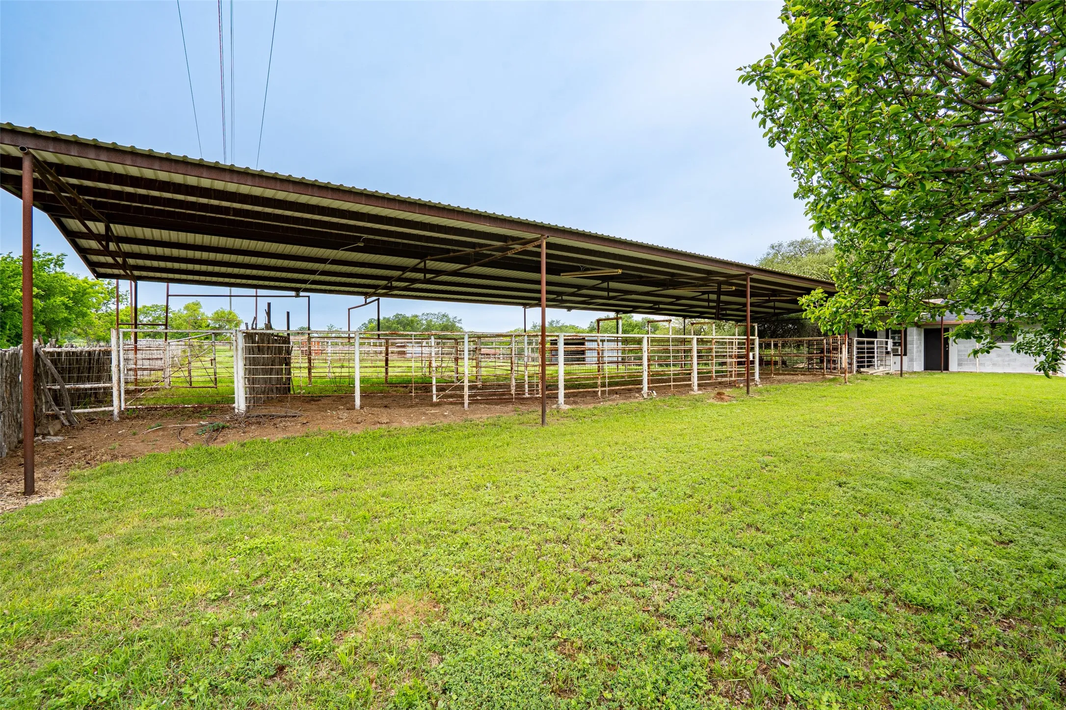 Expansive covered metal structure with multiple fenced pens, featuring a corrugated metal roof and supporting metal posts