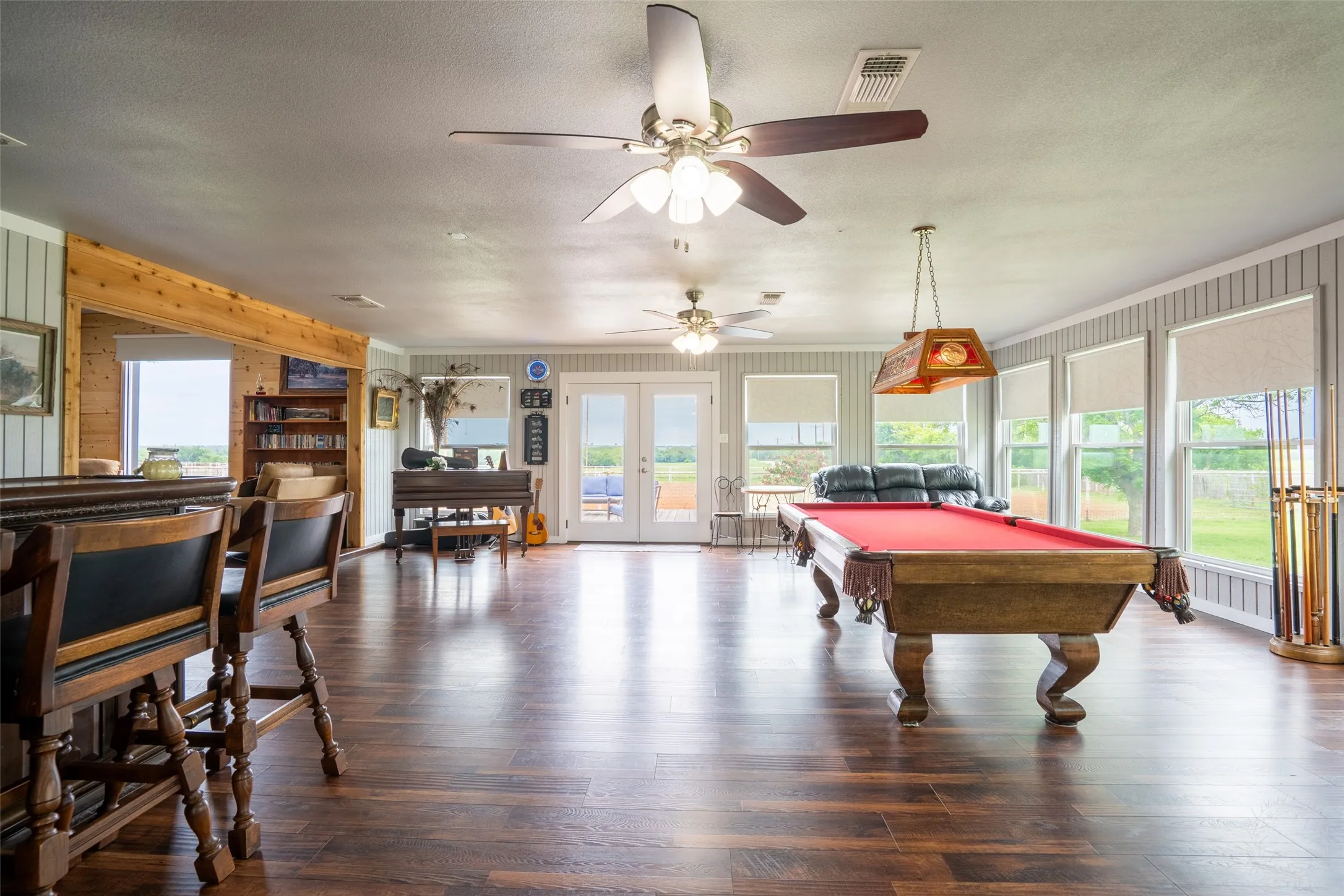 Expansive living space featuring wood-finish flooring, multiple ceiling fans, and abundant natural light from numerous windows