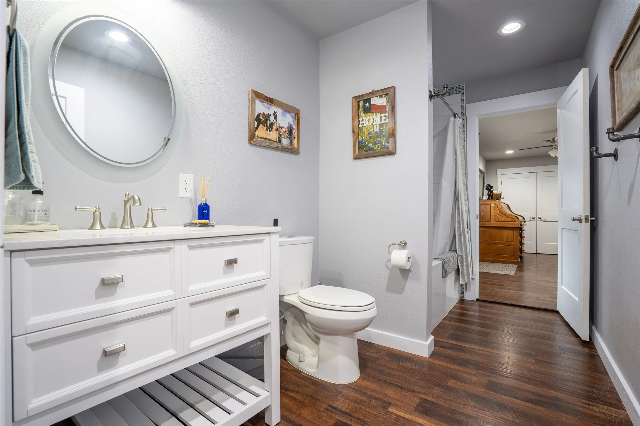 Bathroom featuring a white vanity with brushed nickel hardware, a round mirror, and wood-finish flooring