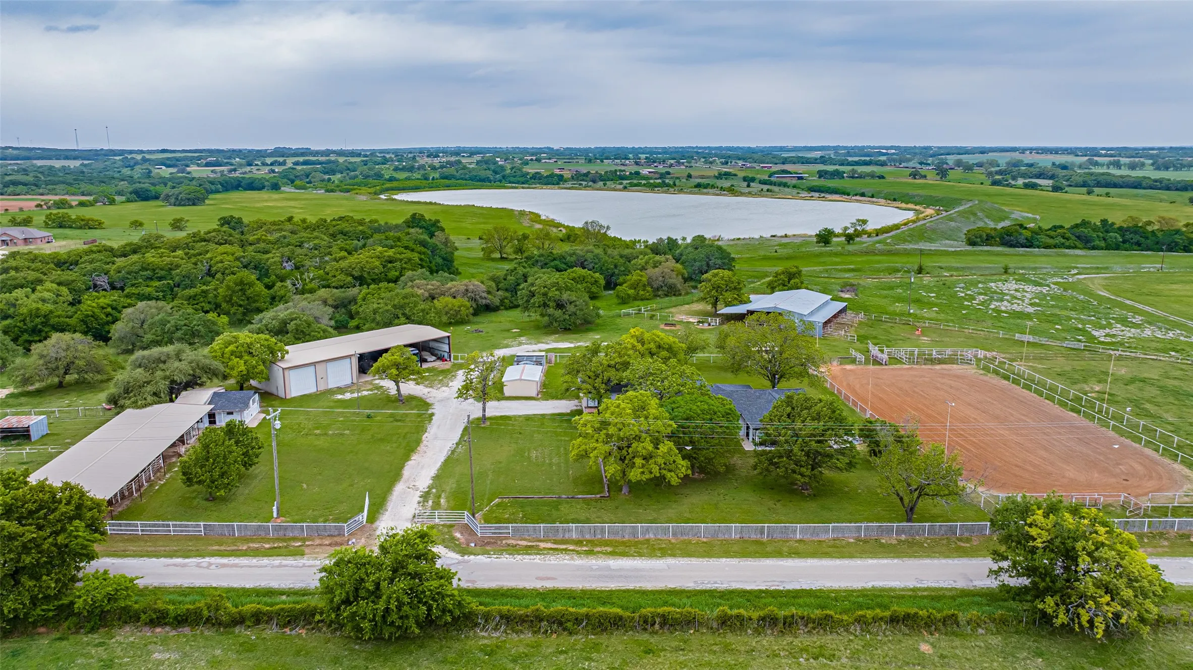 Expansive property featuring a large lake, an equestrian arena, two long barns, a main residence, and additional outbuildings