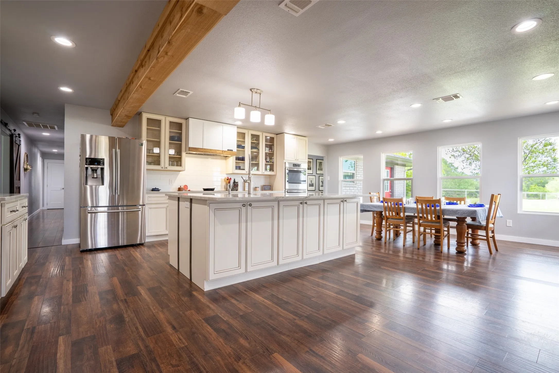 Open-concept living area featuring wood-finish flooring, a kitchen island with built-in cabinetry, stainless steel appliances, and abundant natural light from multiple windows