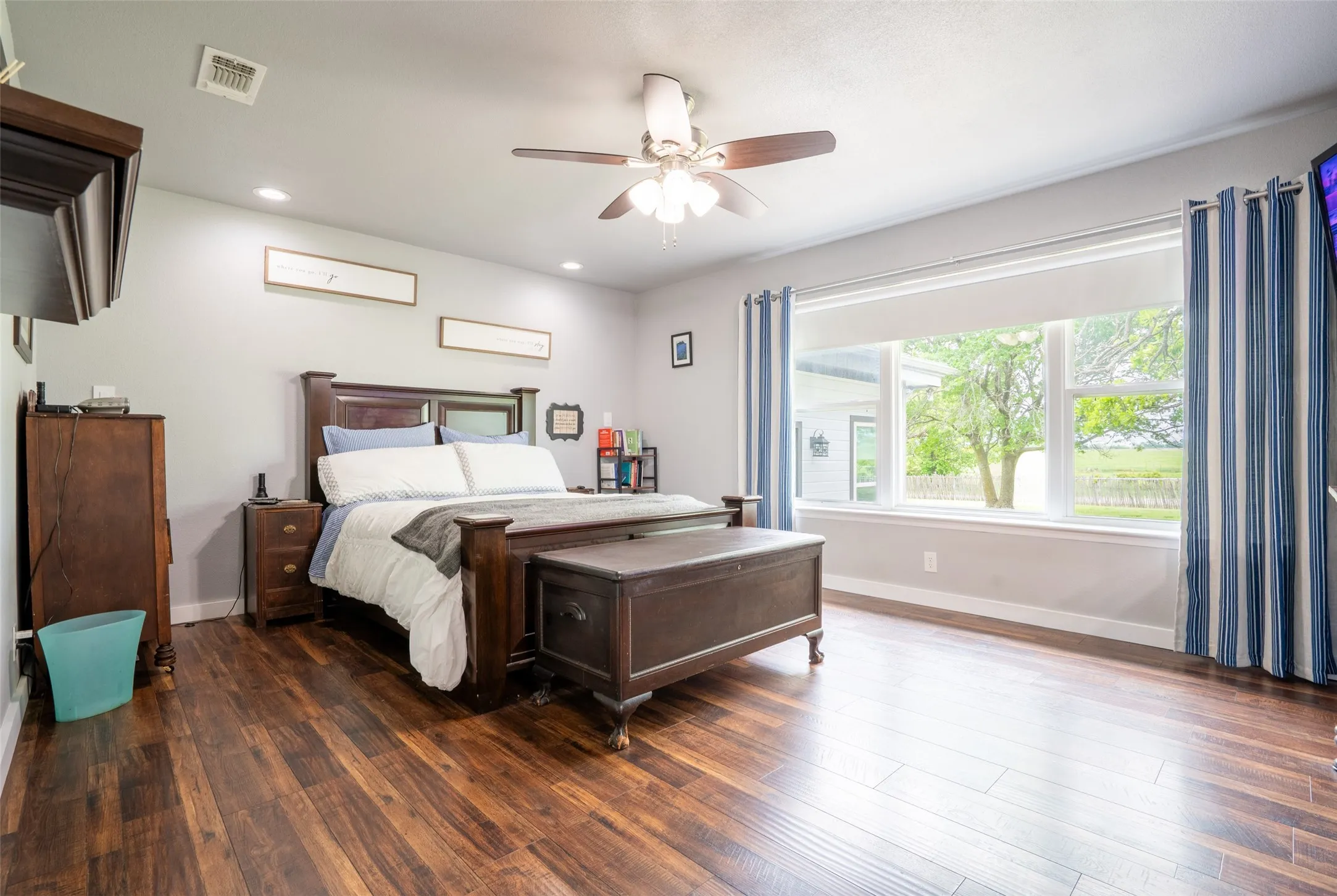 Master bedroom retreat featuring wood-finish flooring, a wide window with a white frame, recessed lighting, and a ceiling fan with integrated lighting