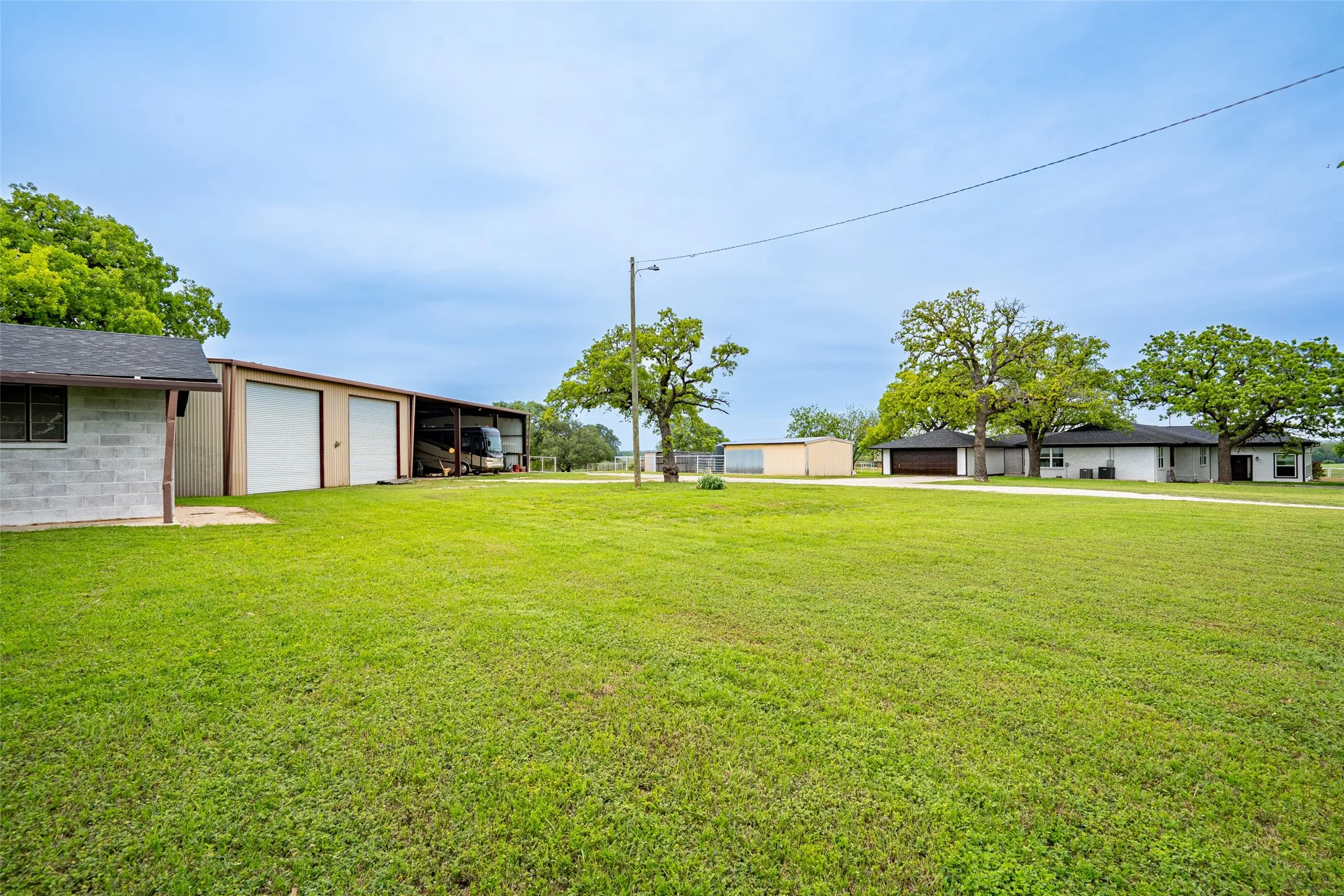 Expansive green space featuring multiple outbuildings, mature trees, and a distant single-story dwelling