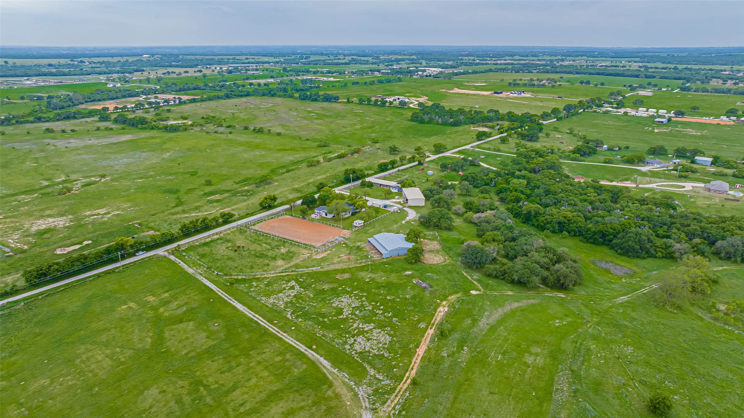 Expansive acreage featuring a fenced riding arena, multiple outbuildings, and a tree-lined perimeter