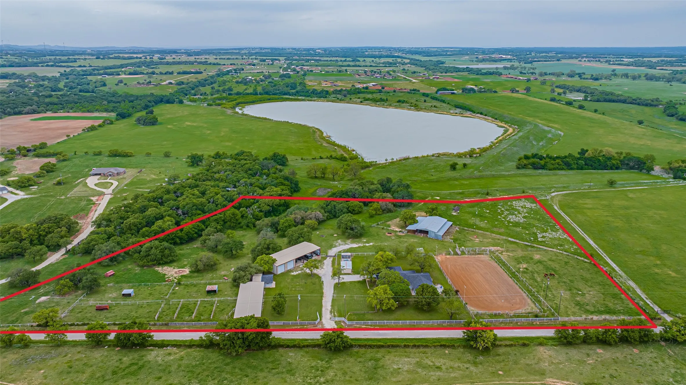 Expansive agricultural property featuring a large natural body of water, multiple outbuildings, an equestrian riding arena, and substantial green space