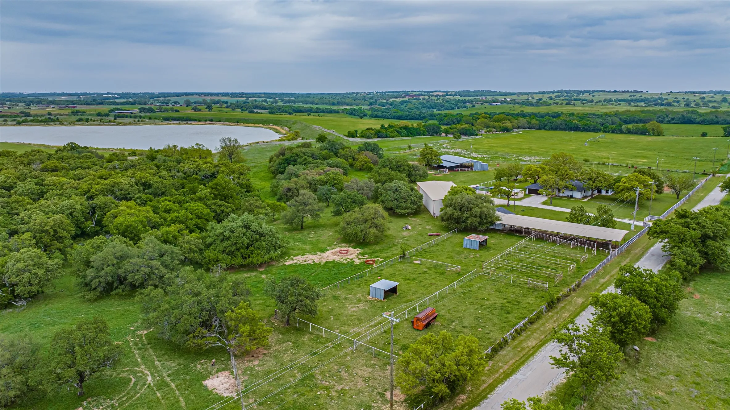 Expansive rural property featuring a large lake, verdant tree coverage, multiple pastures, a substantial barn, and agricultural fencing