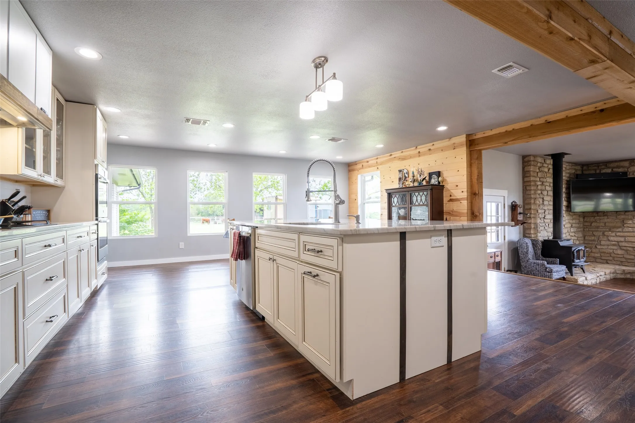 Spacious kitchen featuring a large central island with a sink, light-toned cabinetry, and dark wood-finish flooring