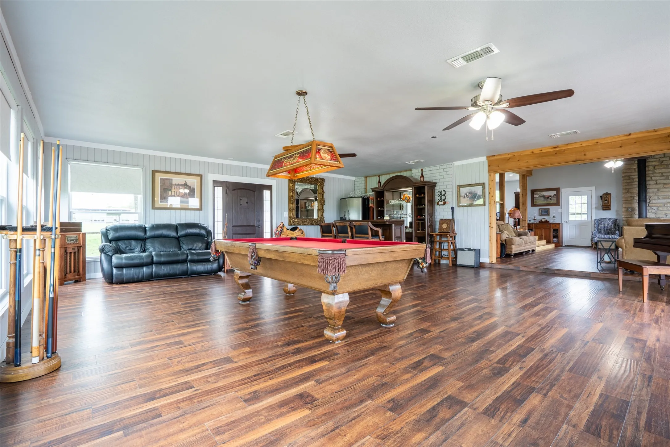 Spacious game room featuring wood-finish flooring, light grey wainscoting, an ornate entry door, and exposed wood beam accents