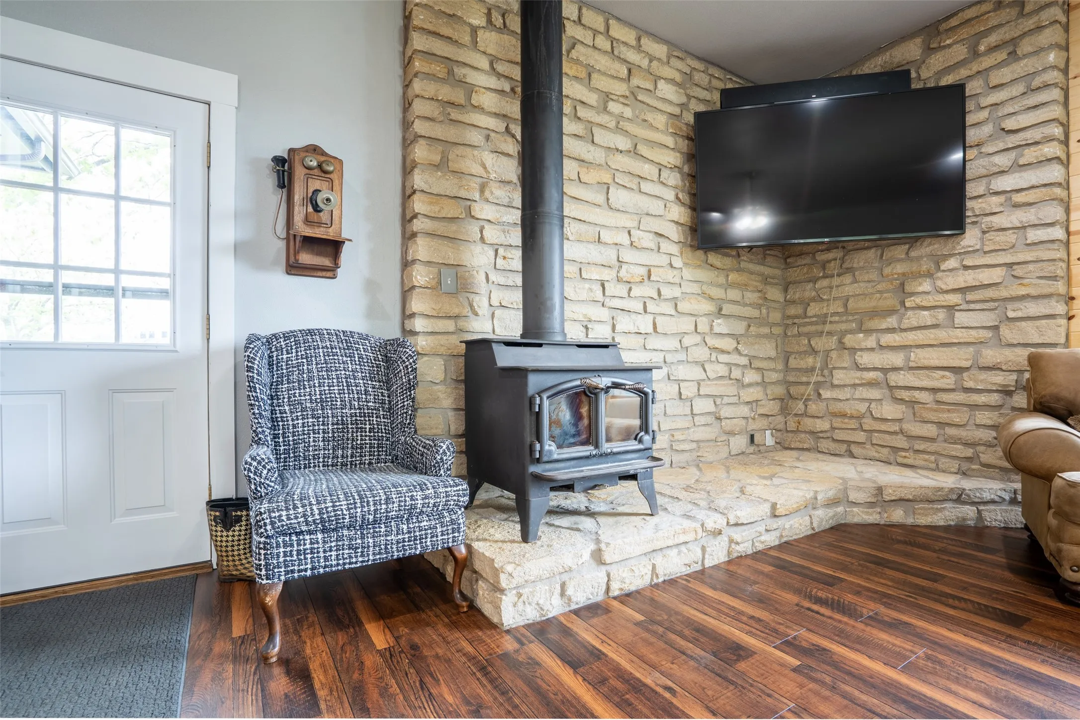 Wood-finish flooring paired with a stone fireplace featuring a wood-burning stove with a stone hearth