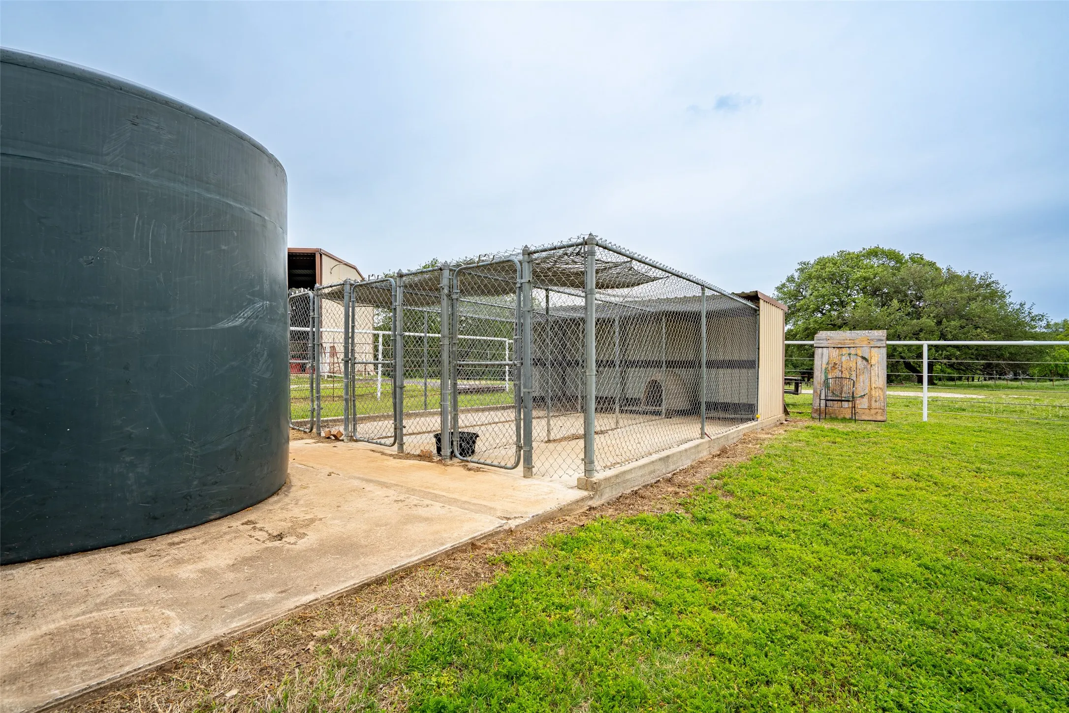 Outdoor chain-link kennel structure on a concrete pad with an adjacent large dark-colored tank