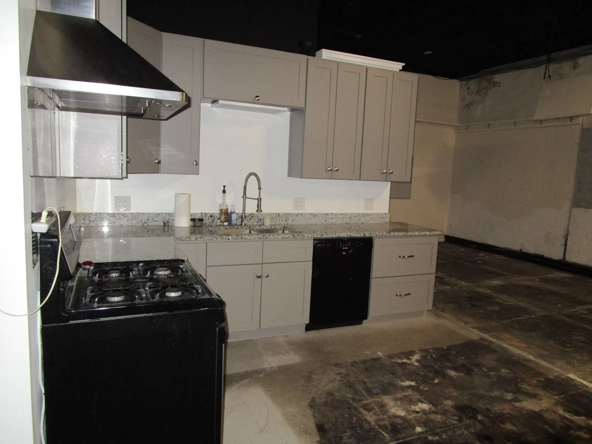Gray cabinetry with brushed nickel hardware, speckled countertops, stainless steel range hood, black range, and black dishwasher