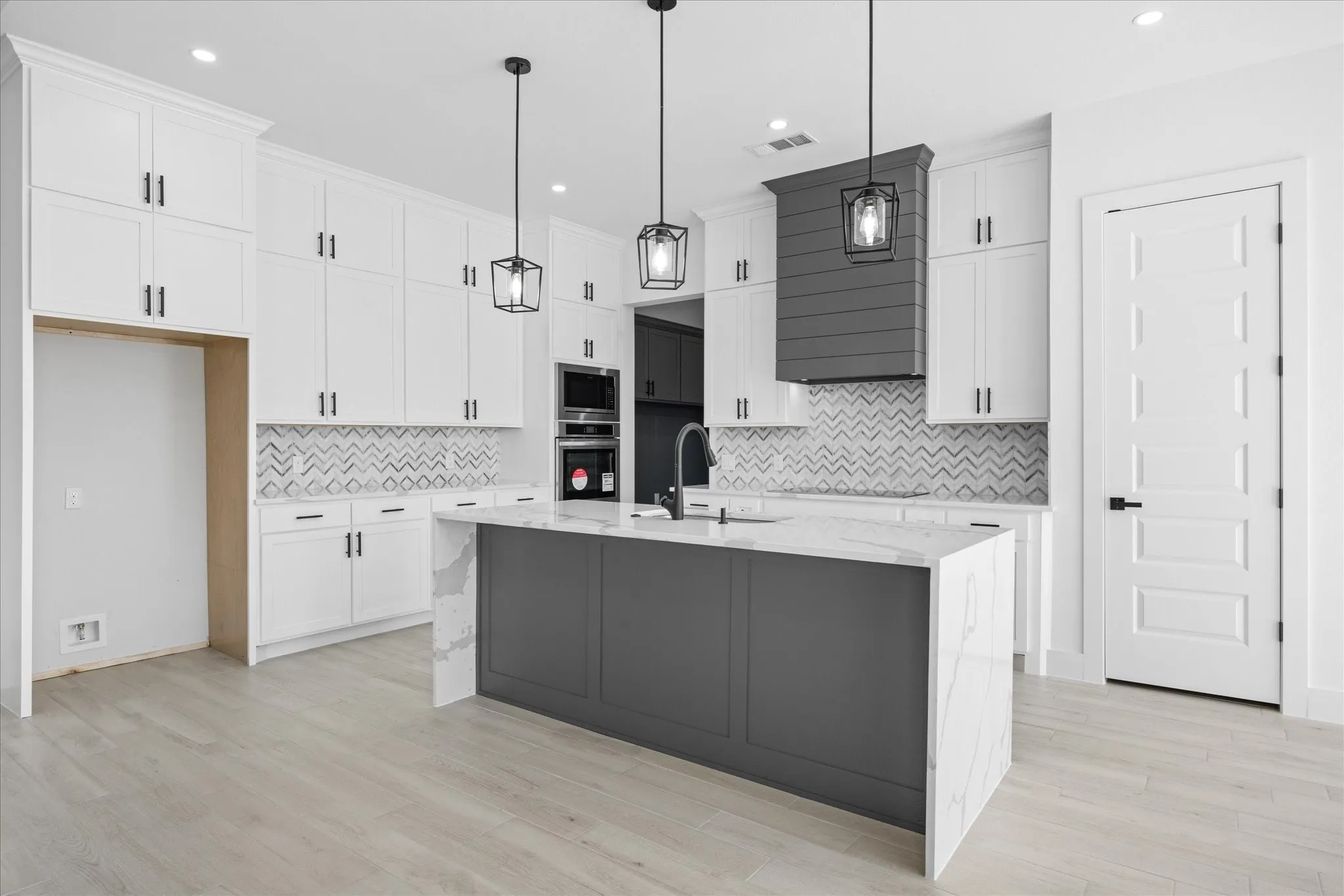 Kitchen featuring a waterfall island with stone countertop, white shaker cabinetry, patterned tile backsplash, built-in double oven, and wood-finish flooring