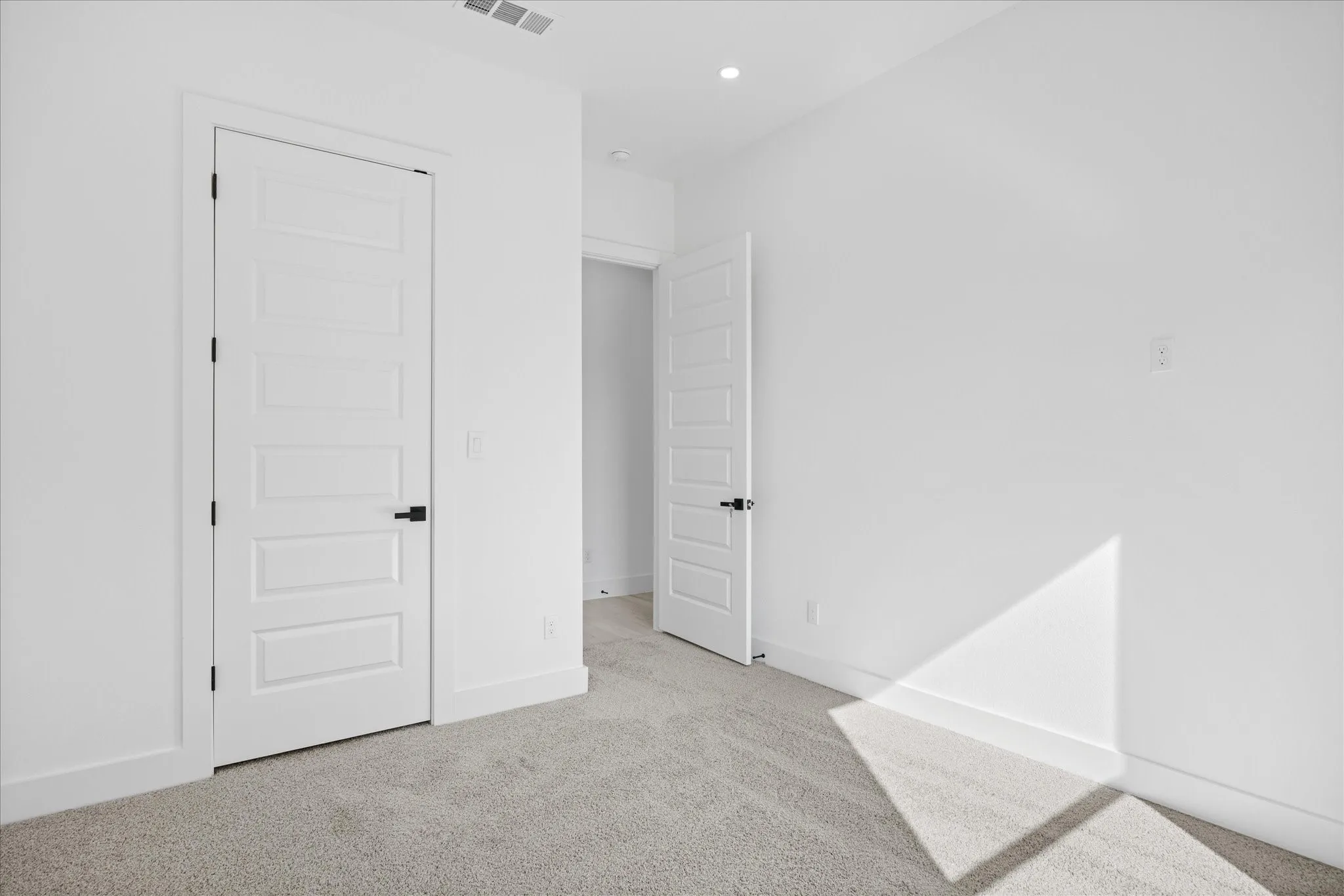 Carpeted Master/owner good size bedroom with white walls, baseboards, and a modern five-panel door featuring a matte black handles/hardwares