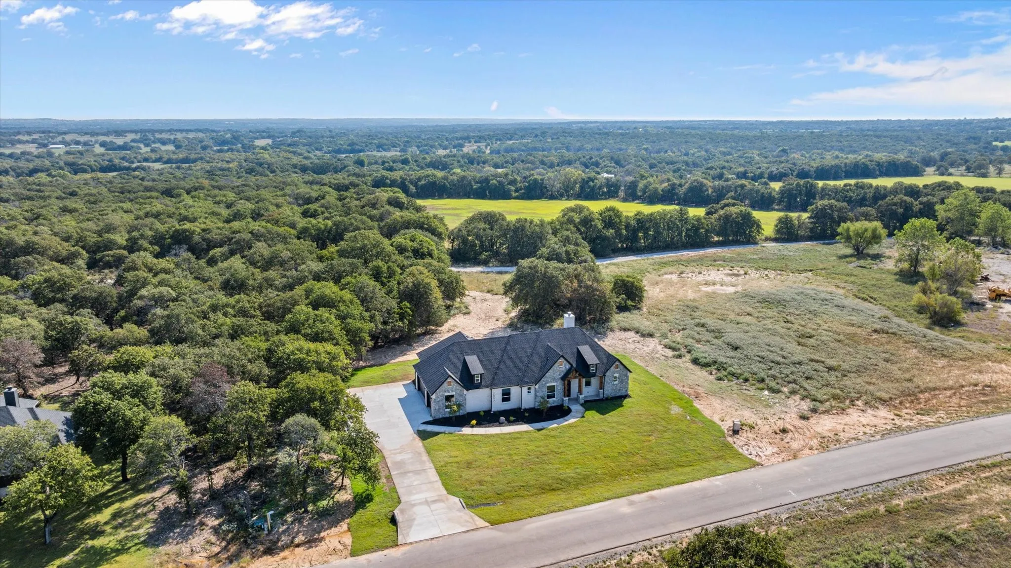Aerial perspective showcasing a modern single-story residence with a dark shingle roof and light-colored stone and brick exterior