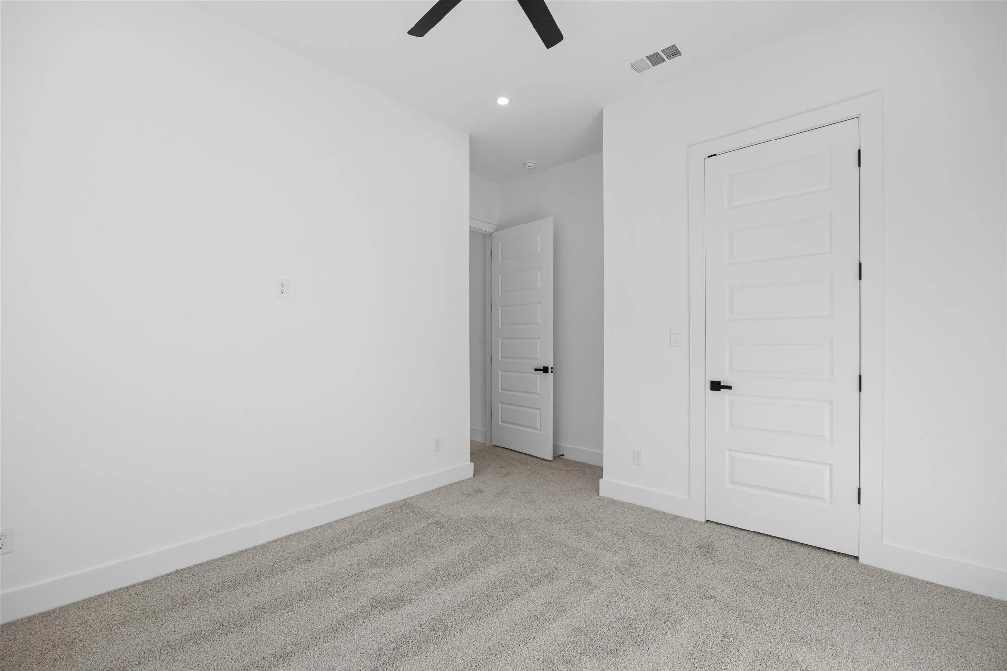 Spacious Kids room featuring light gray carpet, crisp white walls, contemporary white five-panel doors with matte black hardware, and a ceiling fan with integrated lighting
