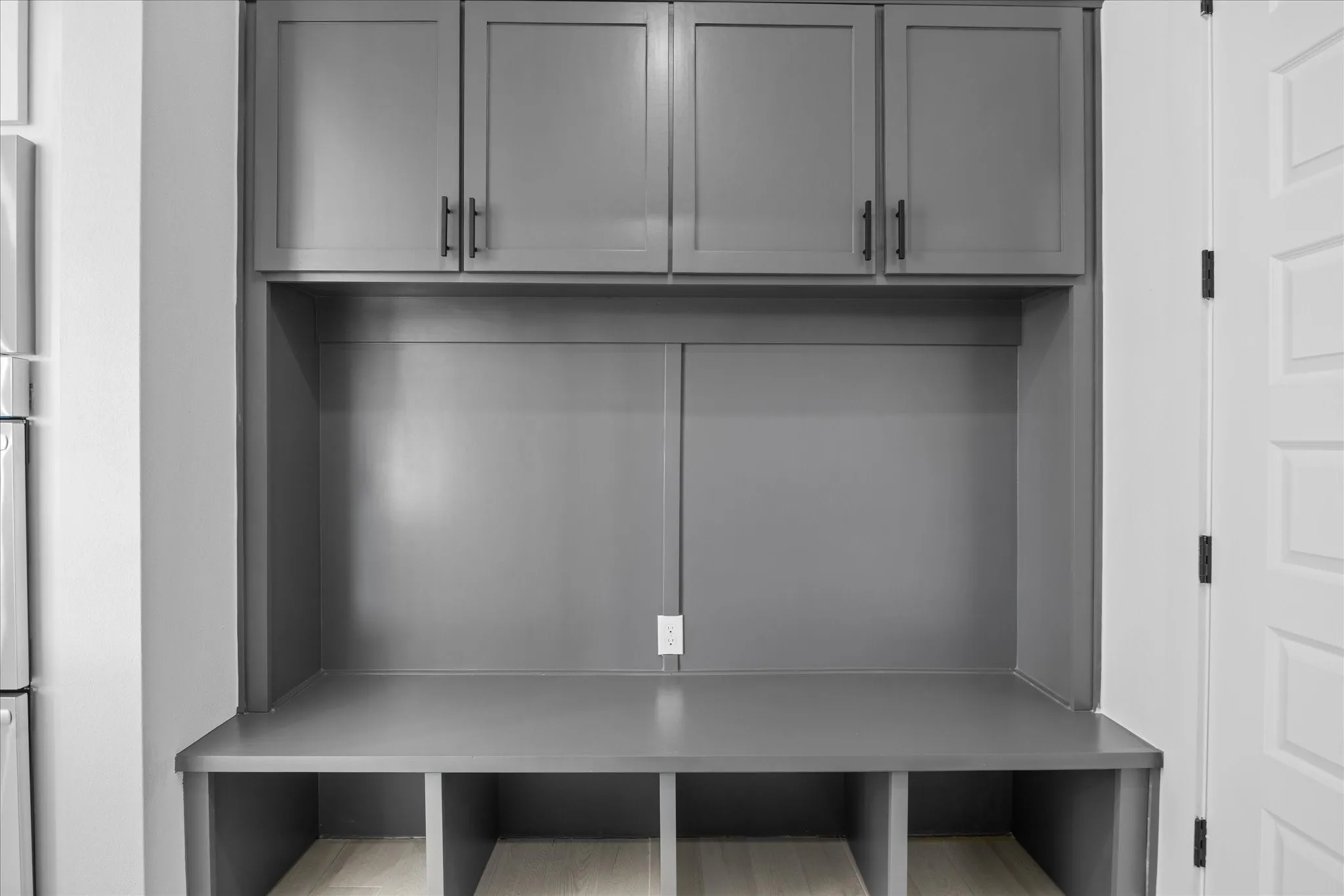 Built-in mudroom station featuring grey shaker-style cabinetry with matte black hardware, integrated bench seating, and open storage cubbies below
